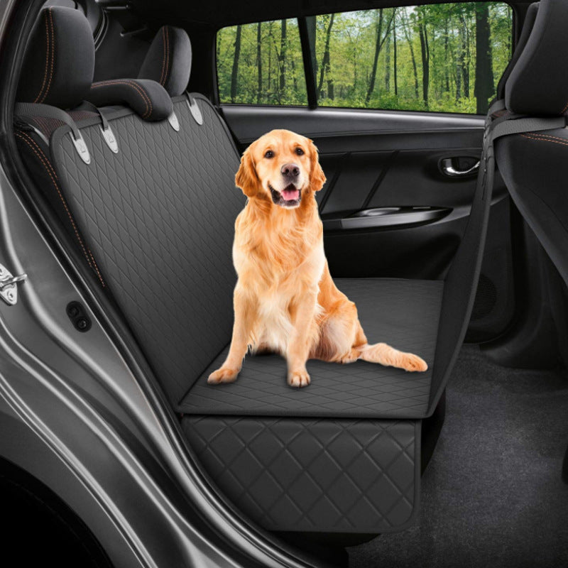 Dog sitting on a black car seat cover in a vehicle with a forest view outside.