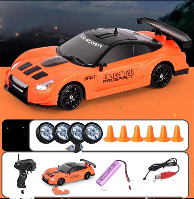 Orange toy car with black details on an orange background, accompanied by remote control, battery, and cones.