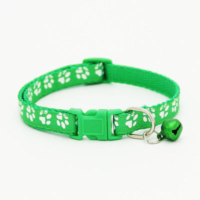 Green cat collar with white paw prints and a bell on a white background