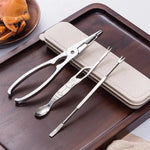 Set of metal seafood tools on a wooden tray with a beige case.