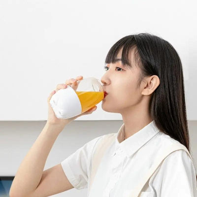 Woman drinking orange juice from a white cup against a plain background