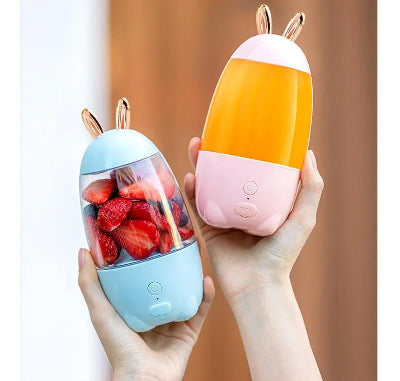 Two portable juicers, one blue and one pink, held by a hand with a blurred background.