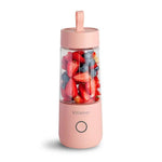Portable blender with pink body and clear lid filled with fruits on a white background