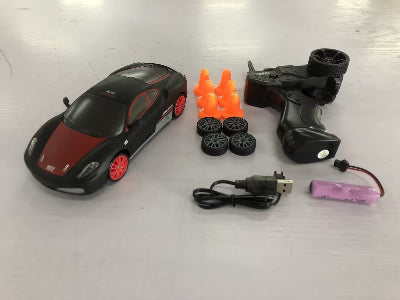 Toy car with accessories including a remote control, battery, and spare wheels on a white surface.