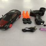 Toy car with accessories including a remote control, battery, and spare wheels on a white surface.