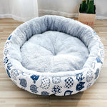 Round pet bed with blue and white cat pattern on a wooden floor.