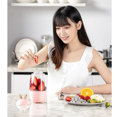 Woman in a kitchen preparing a smoothie with a blender, surrounded by fruits.