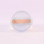 Clear container with a gold-colored object on a light purple background