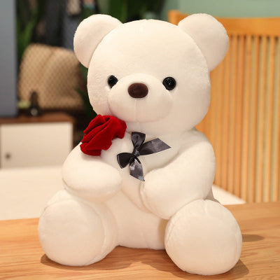 White teddy bear with a red rose and black bow tie on a wooden surface.