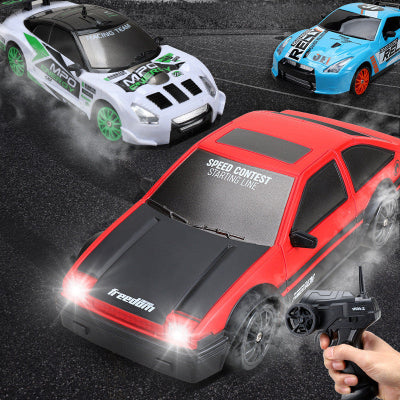Three toy cars with racing decals on a track, one with a remote control held by a hand.