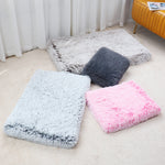 Three fluffy cushions in gray, pink, and white on a light-colored floor.