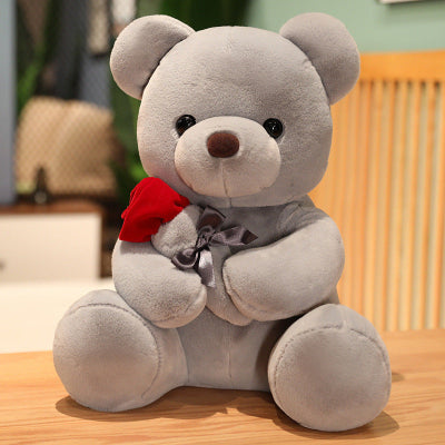 Gray teddy bear with a red bow tie on a wooden surface
