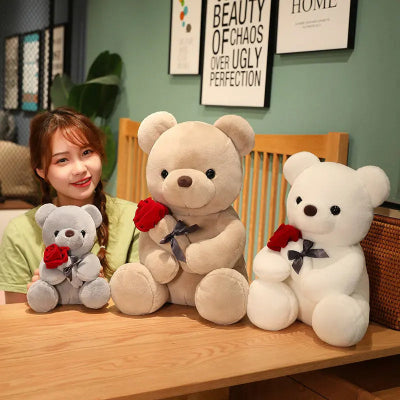 Woman sitting with three teddy bears on a table in a room with framed pictures on the wall.