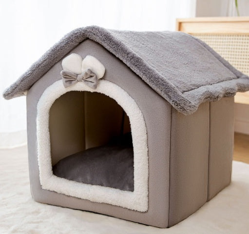 Gray pet house with a bow on top, sitting on a light-colored surface.