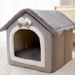 Gray pet house with a bow on top, sitting on a light-colored surface.